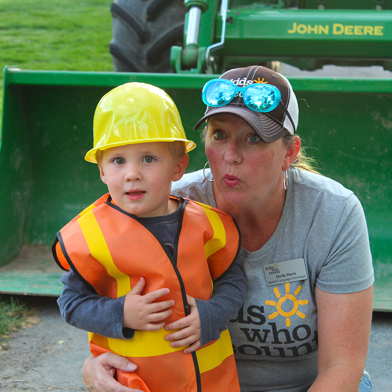 Young child in a hard hat with a Kids Who Count worker